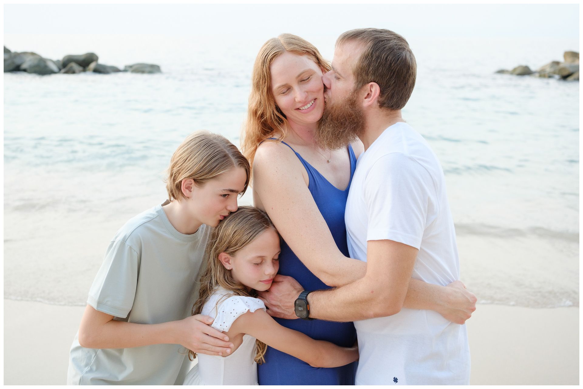A family plays together on a beach, lifting a child in the air while wearing white clothing in black and white photography.