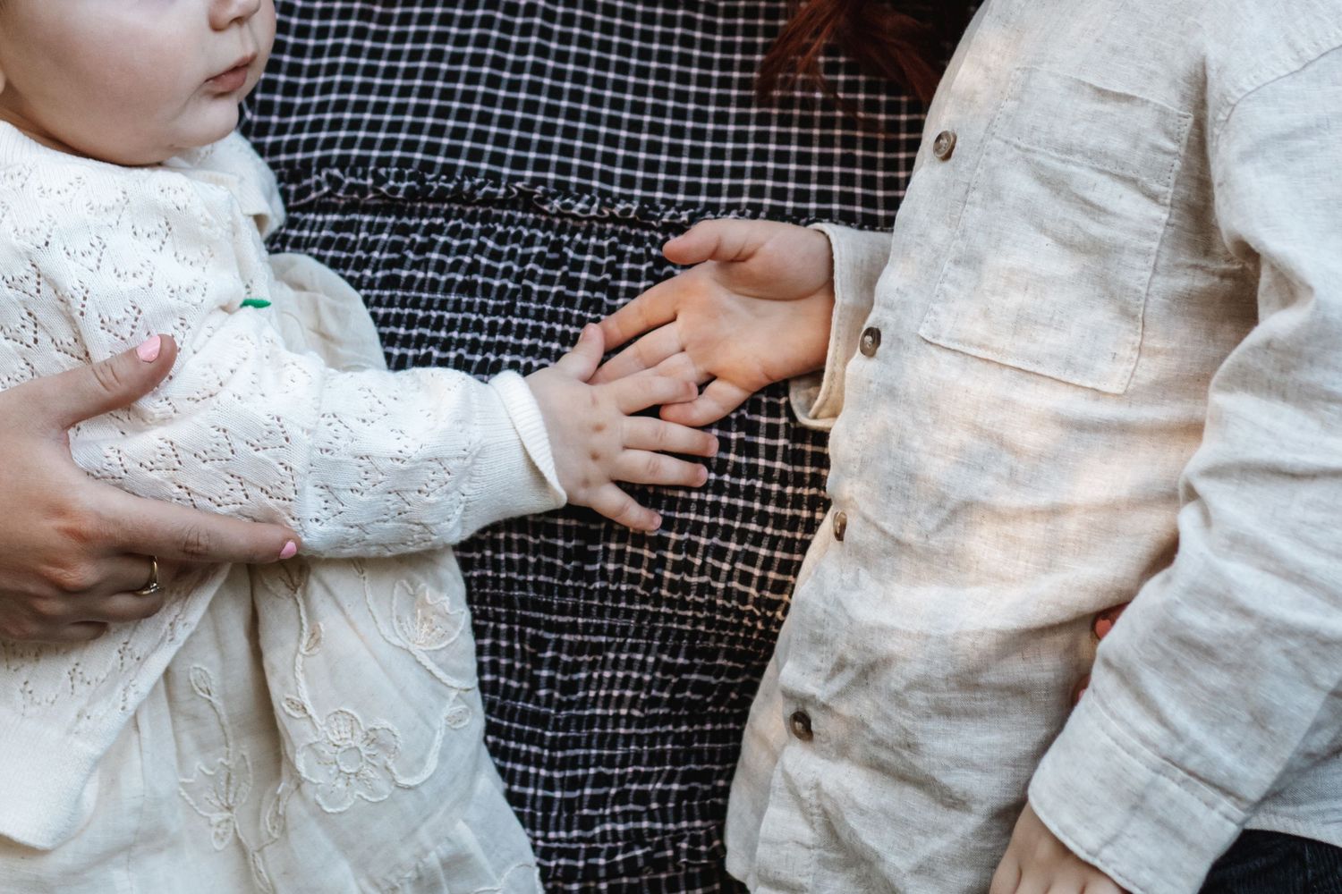Close-up of baby and child hands touching, wearing white and beige outfits, family bonding moment.