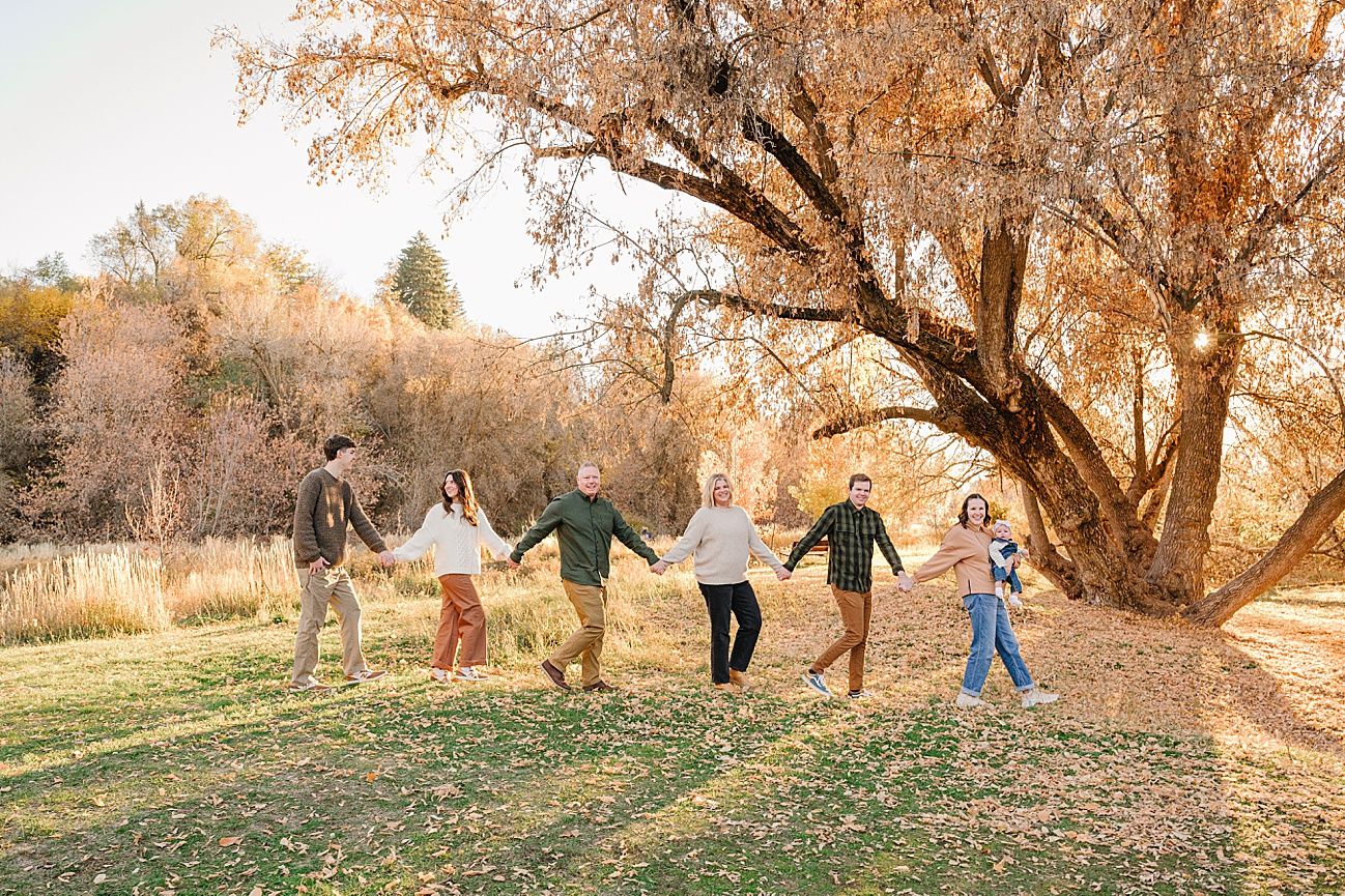 A sequence of silhouetted figures walking through a golden autumn landscape with sunlit trees in the background.