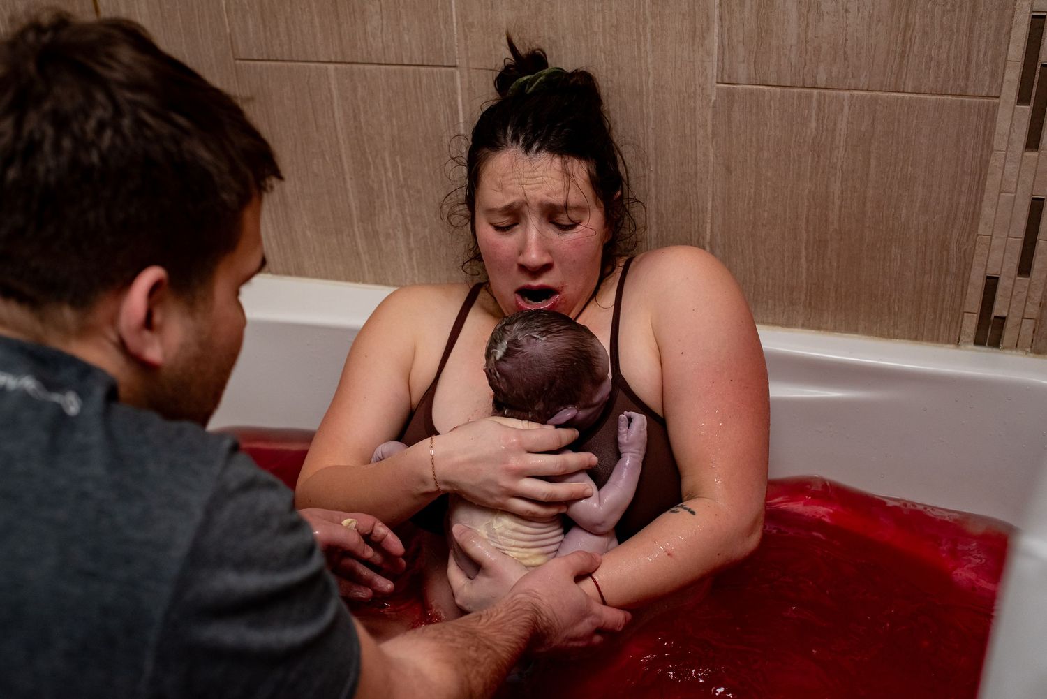 Black and white photo of a woman laboring in a bathtub during a water birth, supported by her partner.