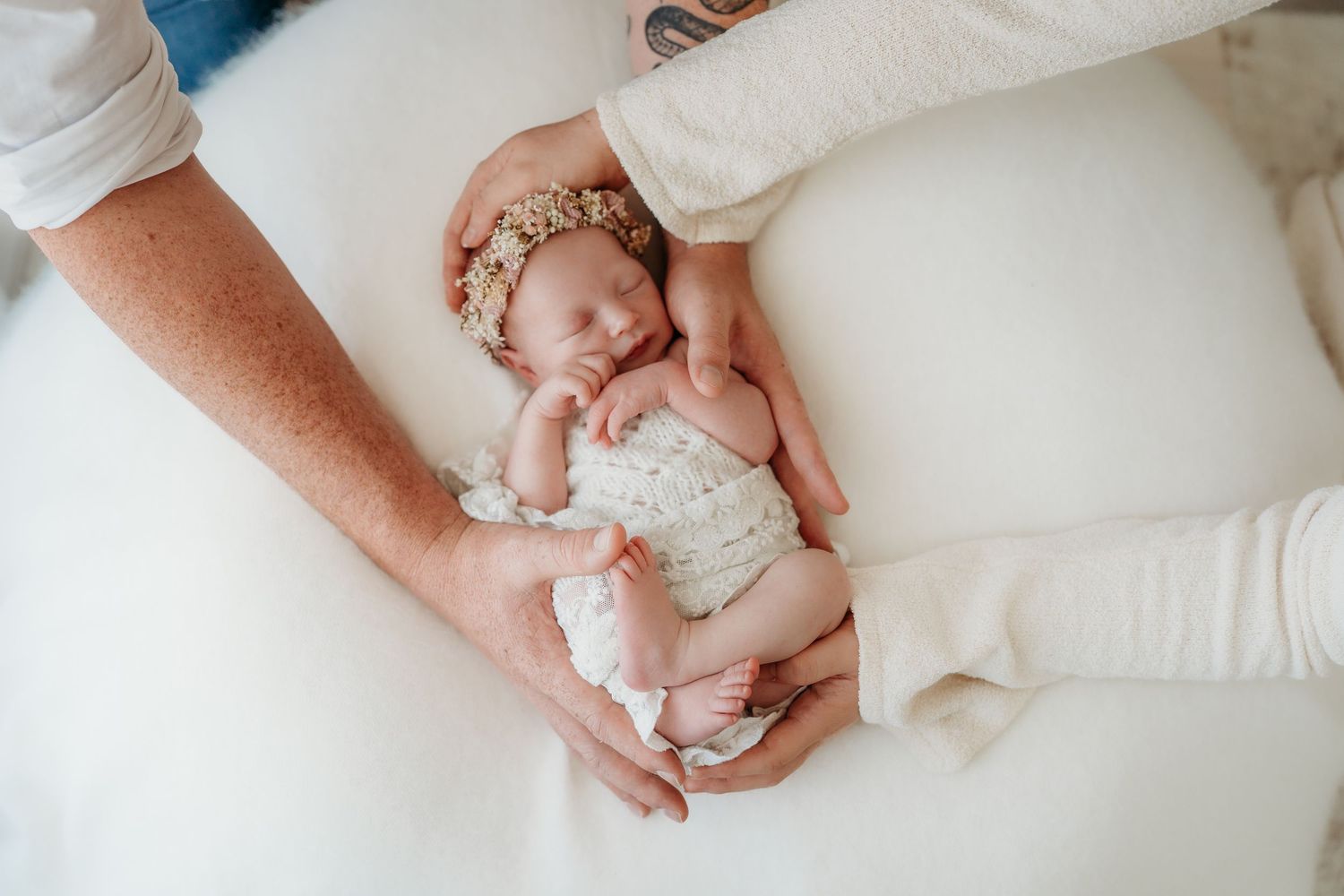Mother in white dress tenderly holds sleeping newborn dressed in knitted beige outfit and headband.