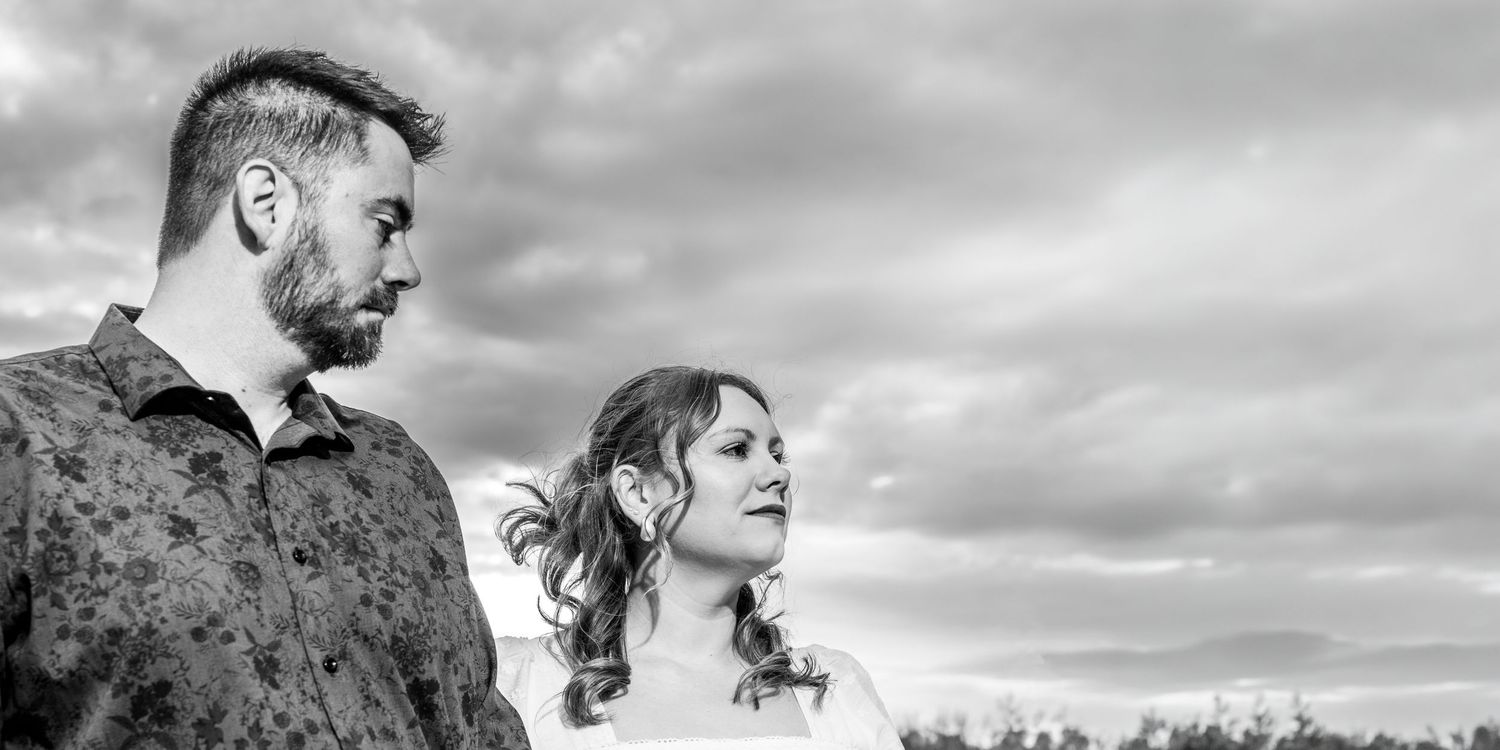 A fiancé looking down lovingly at his girl in front of a dramatic sky in a black and white portrait in Chelsea MI