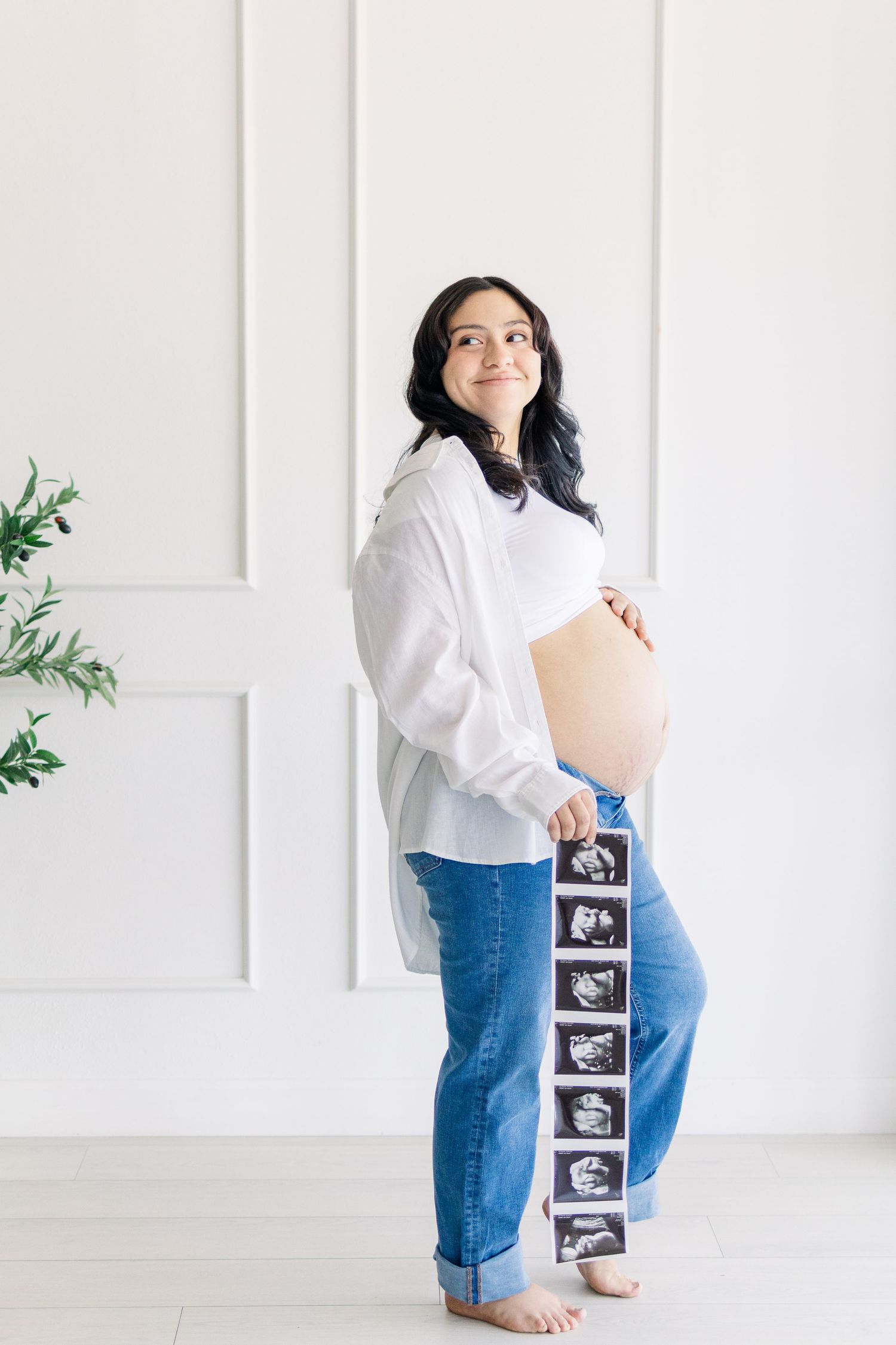 Light and airy maternity photo of a young pregnant mom holding ultrasound and smiling in a studio maternity session