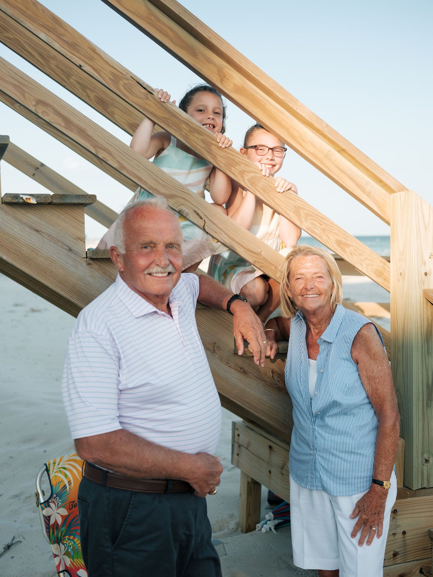 Grandparents smile with two grandchildren on wooden beach stairs at golden hour.