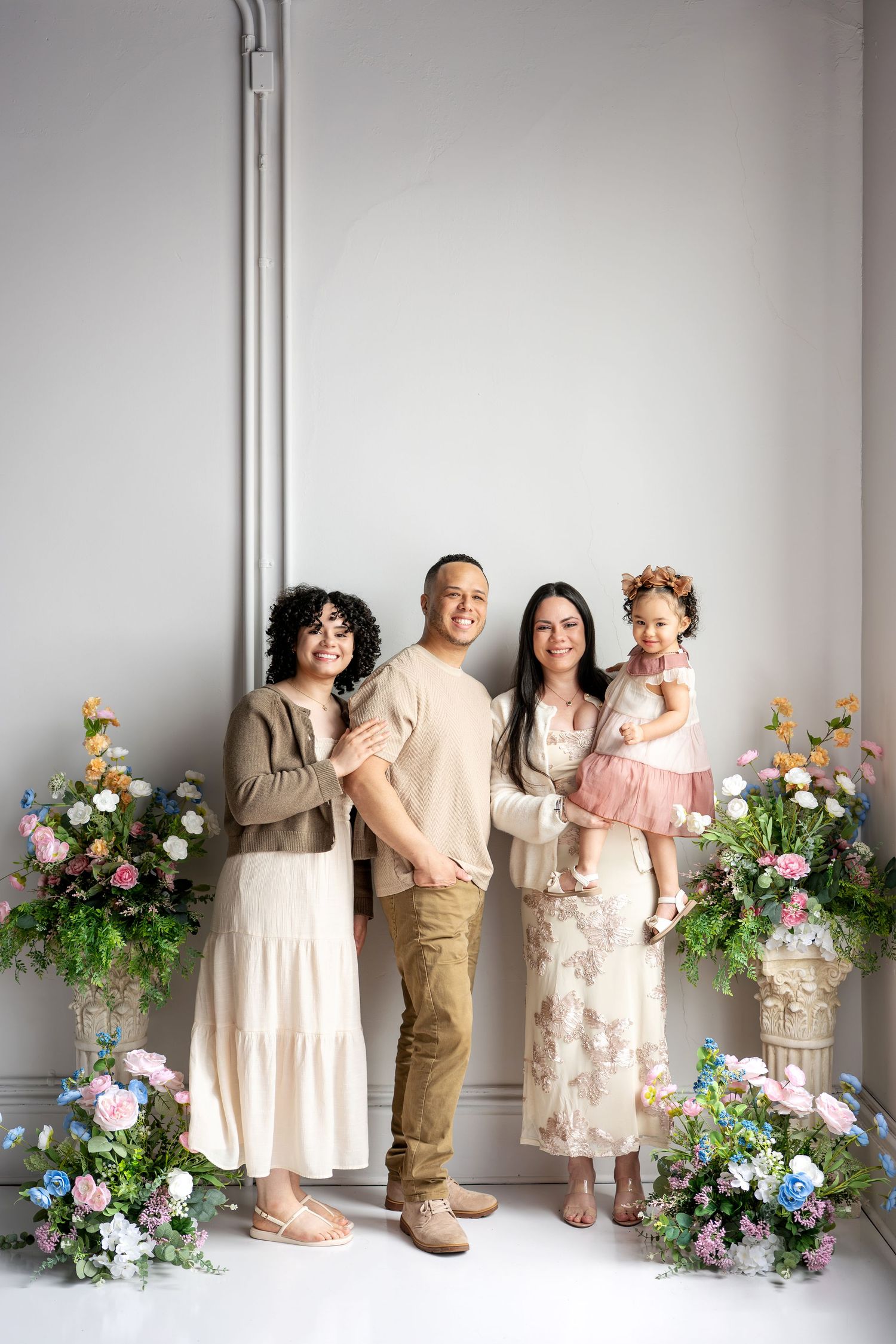 Happy family of four posing with colorful floral arrangements in bright studio.