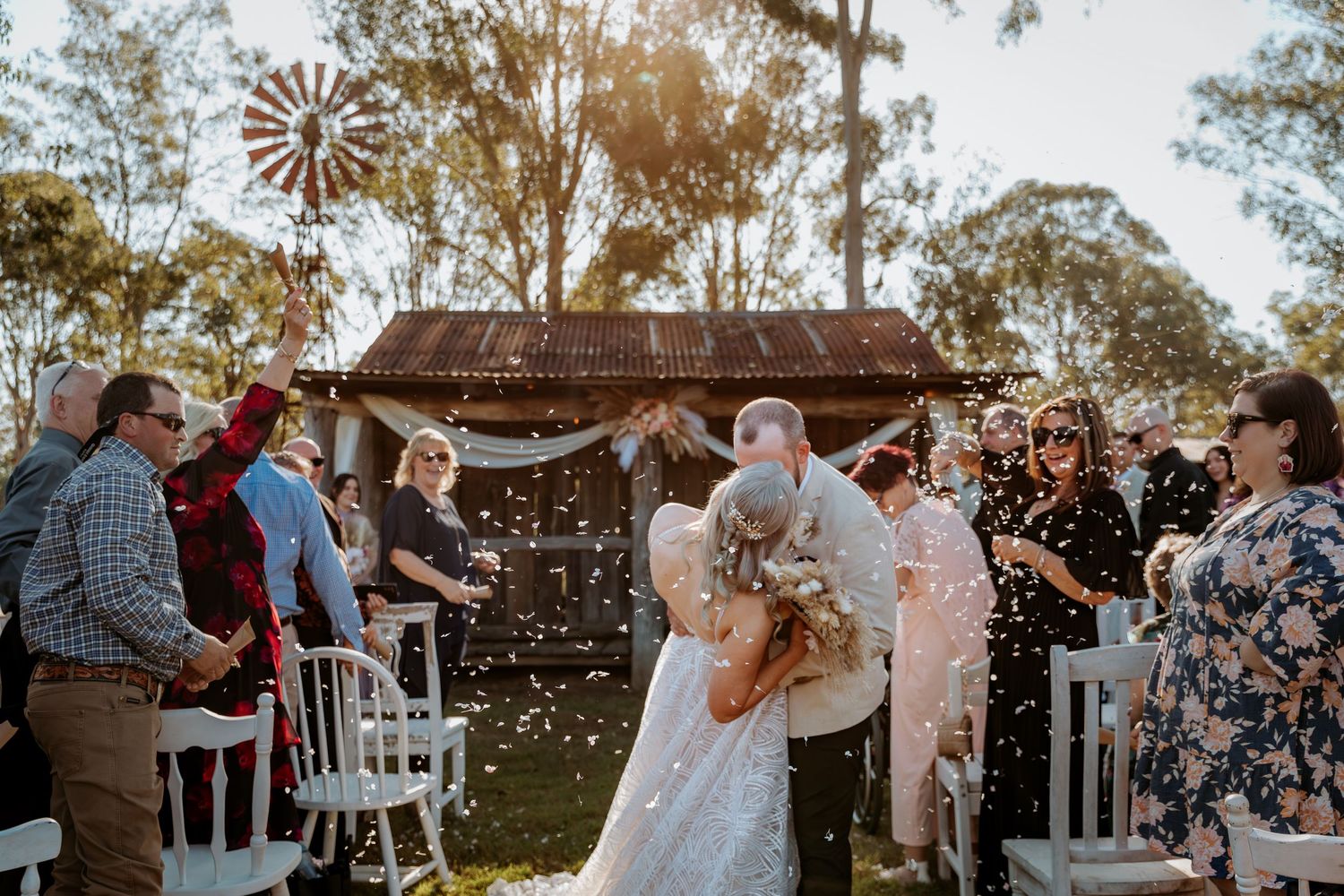 Outdoor wedding ceremony at rustic venue with windmill and natural landscape.