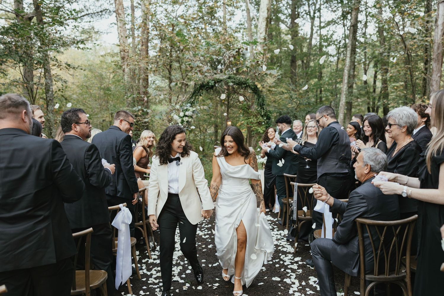 Outdoor wedding ceremony takes place on lawn in front of grand stone castle with Gothic architecture under cloudy skies.