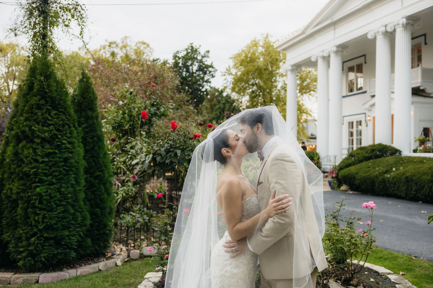 A romantic moment captured between a couple sharing a kiss in front of a grand white columned wedding venue in Naperville Illinois