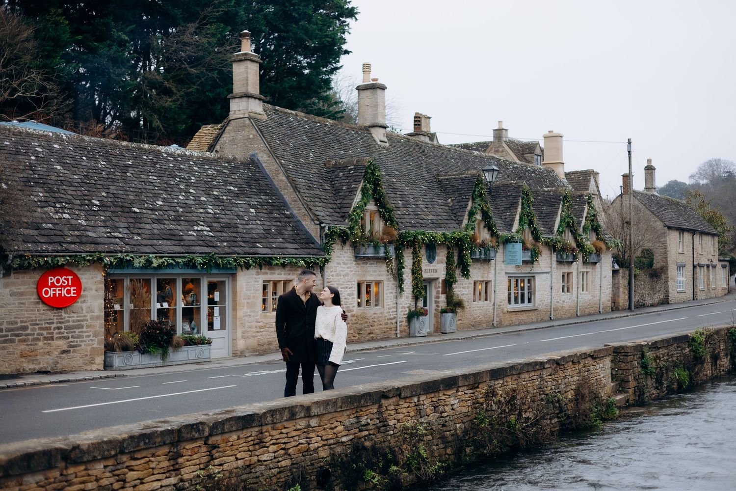 Row of traditional stone cottages line a quiet village street in the Cotswolds on an overcast day.