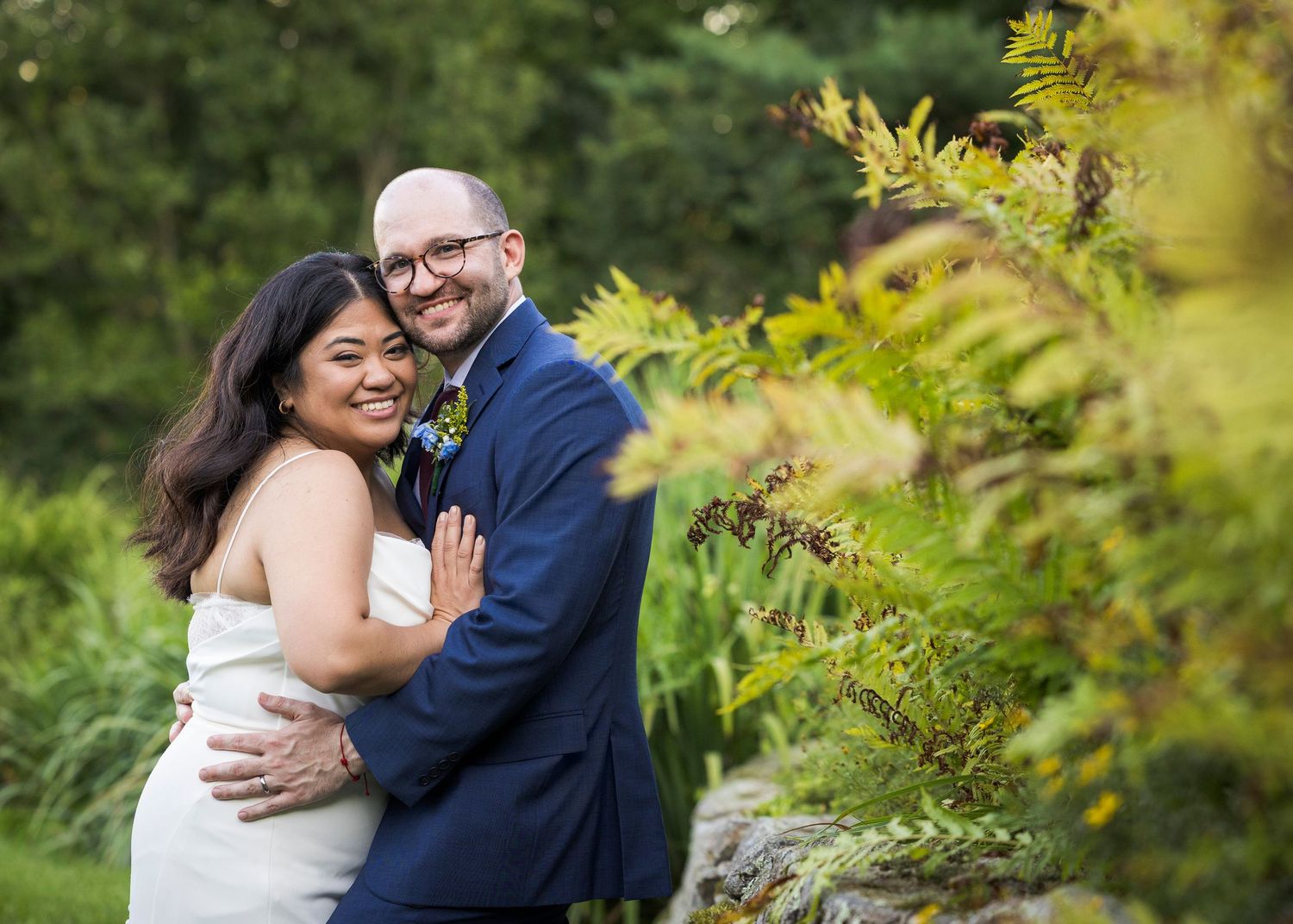 Newlyweds share an intimate moment outdoors with autumn foliage and rustic architecture in background.