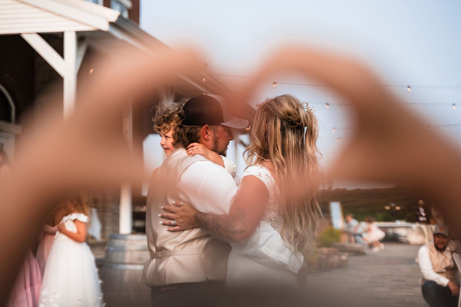 A romantic wedding couple photographed through a heart shape formed by blurred hands in the foreground.