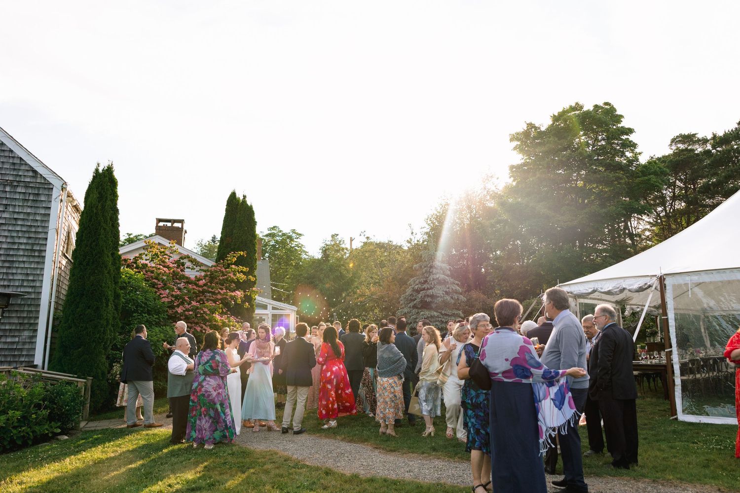 Wedding guests gather on a lawn at sunset during an outdoor reception celebration.