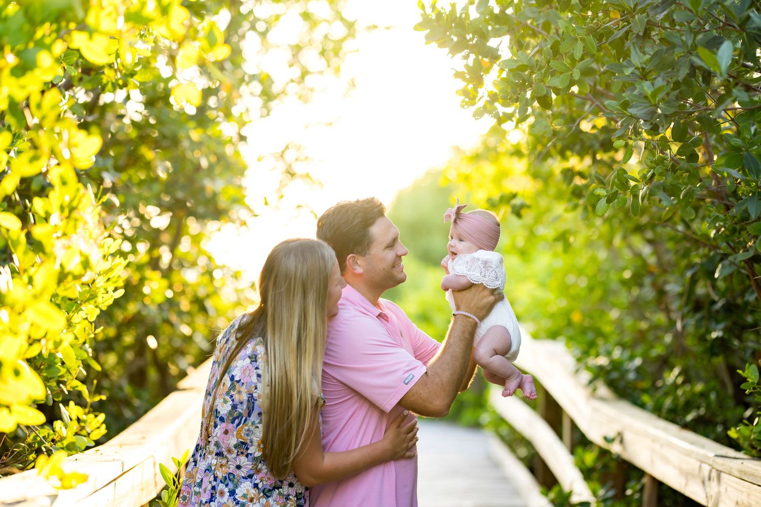 A tender outdoor family moment in a lush garden setting surrounded by sunlit foliage and greenery.