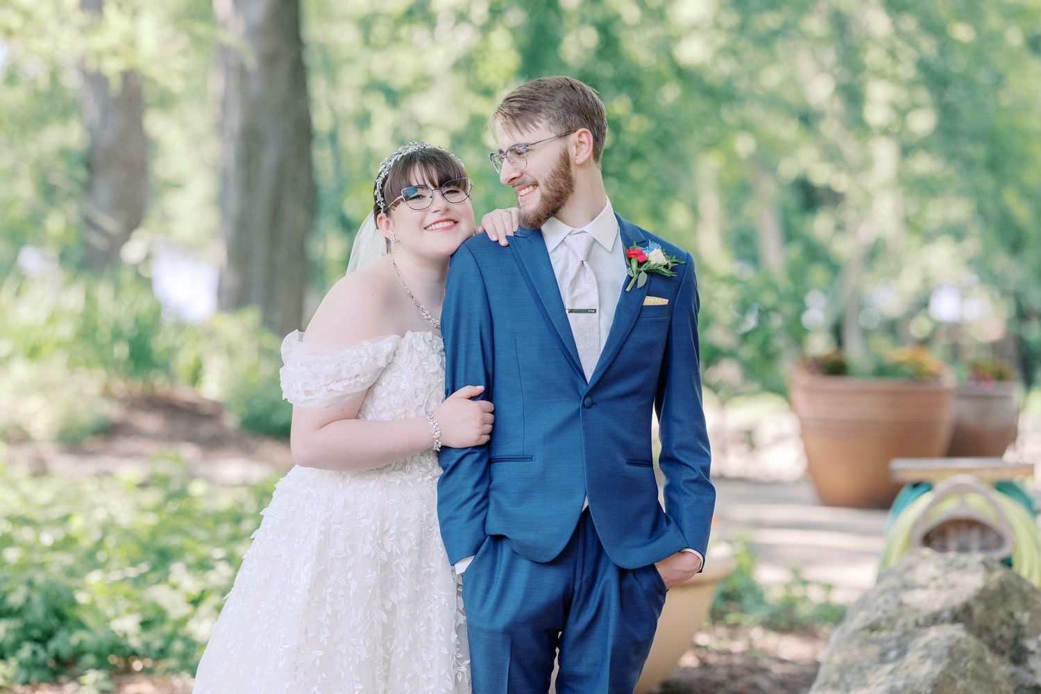A couple in wedding attire embraces in a lush garden setting with natural greenery in the background.