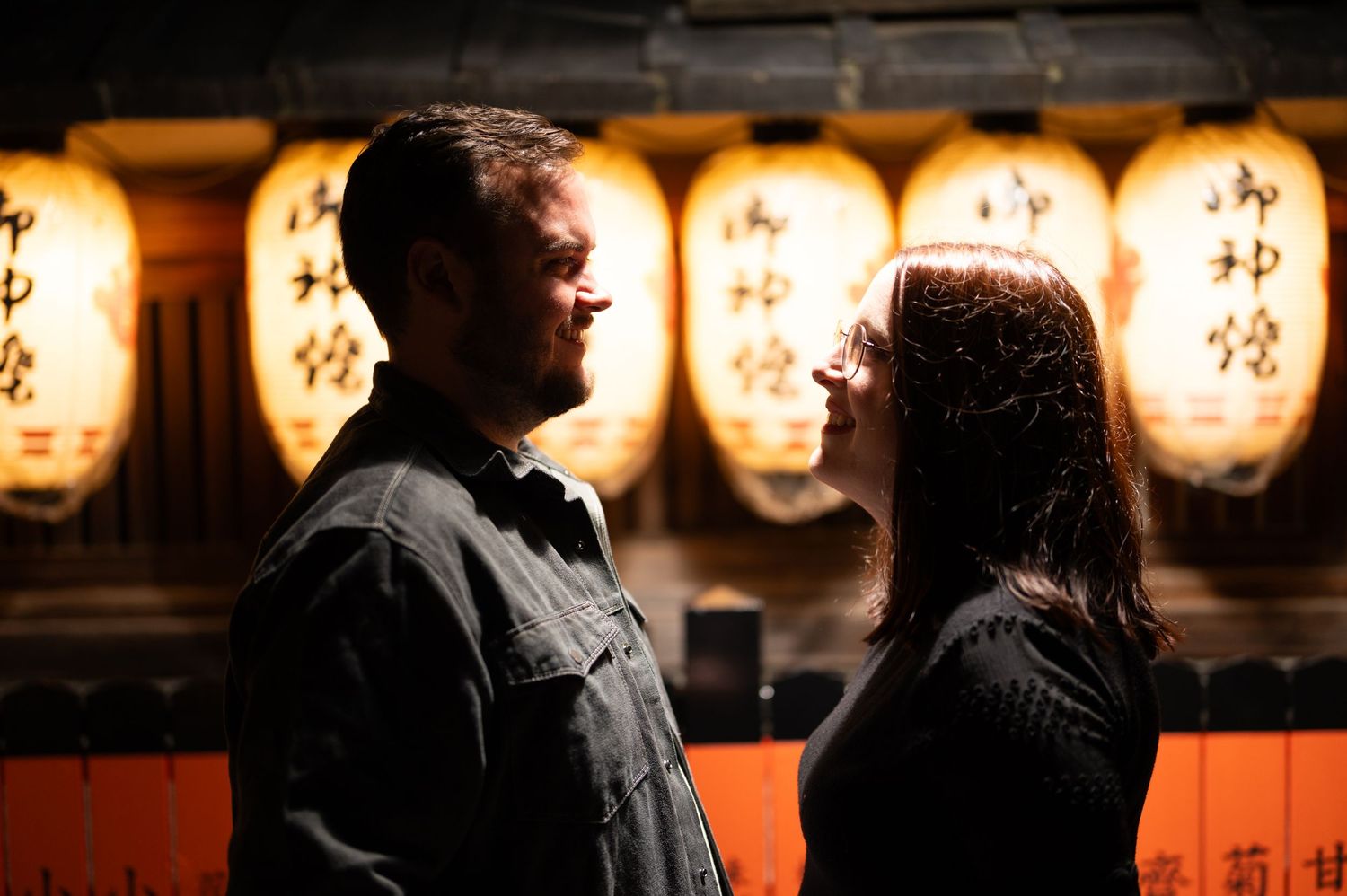 Couple gazing at each other romantically in front of glowing traditional Japanese lanterns at night.