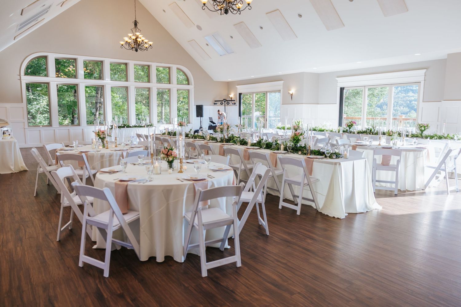 Panoramic view of an elegant white wedding reception venue with round tables and cathedral ceiling windows. Garden in the gorge.