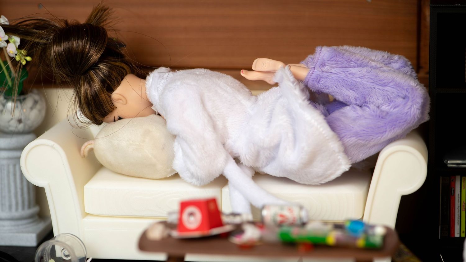 Barbie doll in white dress lying on a miniature sofa in a detailed dollhouse living room scene.