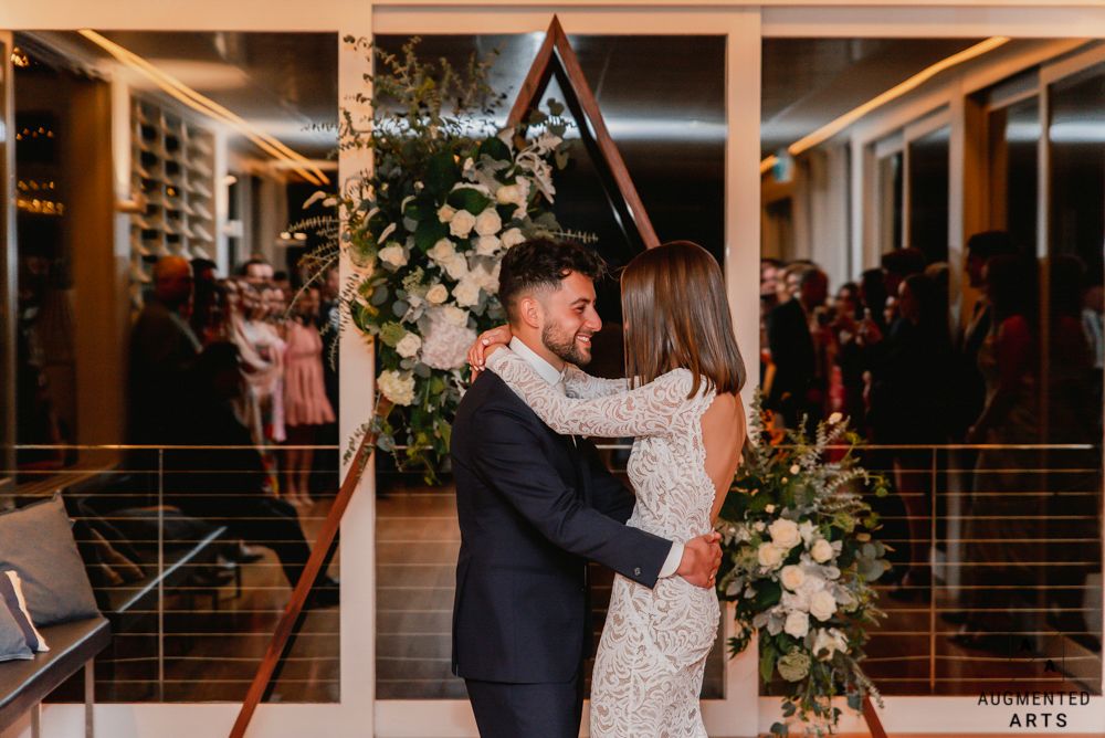 A couple shares an intimate moment during their wedding celebration in a modern venue with warm lighting and floral decorations.