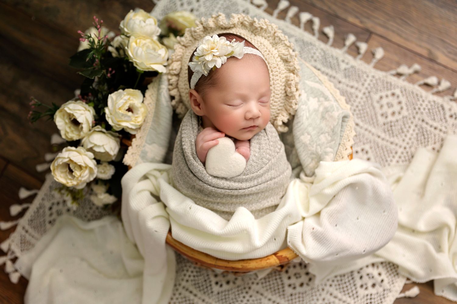 Newborn baby sleeps peacefully on cream lace blankets surrounded by white roses.