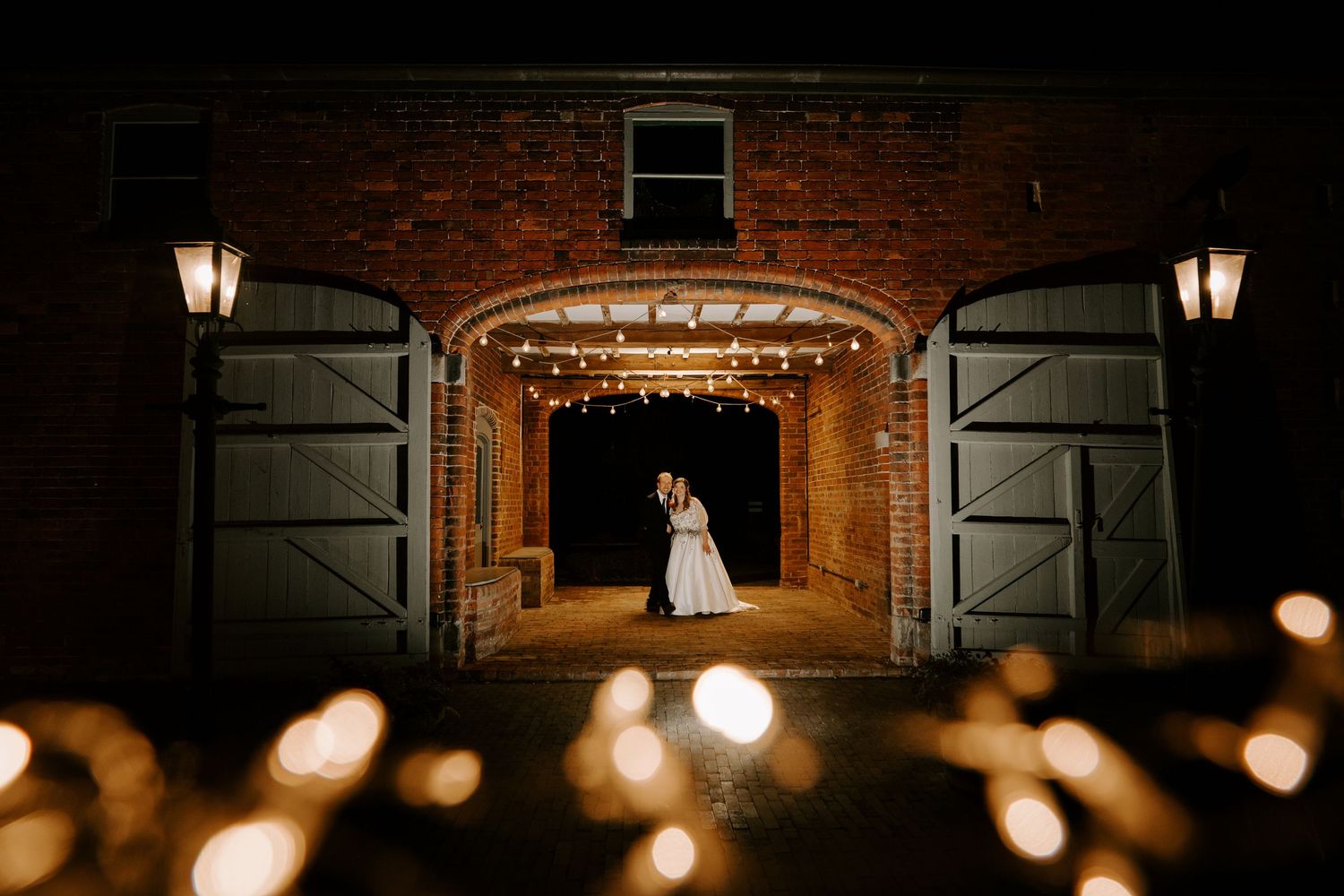 Wedding couple poses among lush greenery and white floral arrangements outdoors.