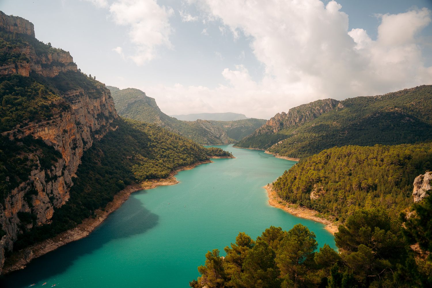 Aerial view of a winding turquoise lake nestled between dramatic mountain cliffs.