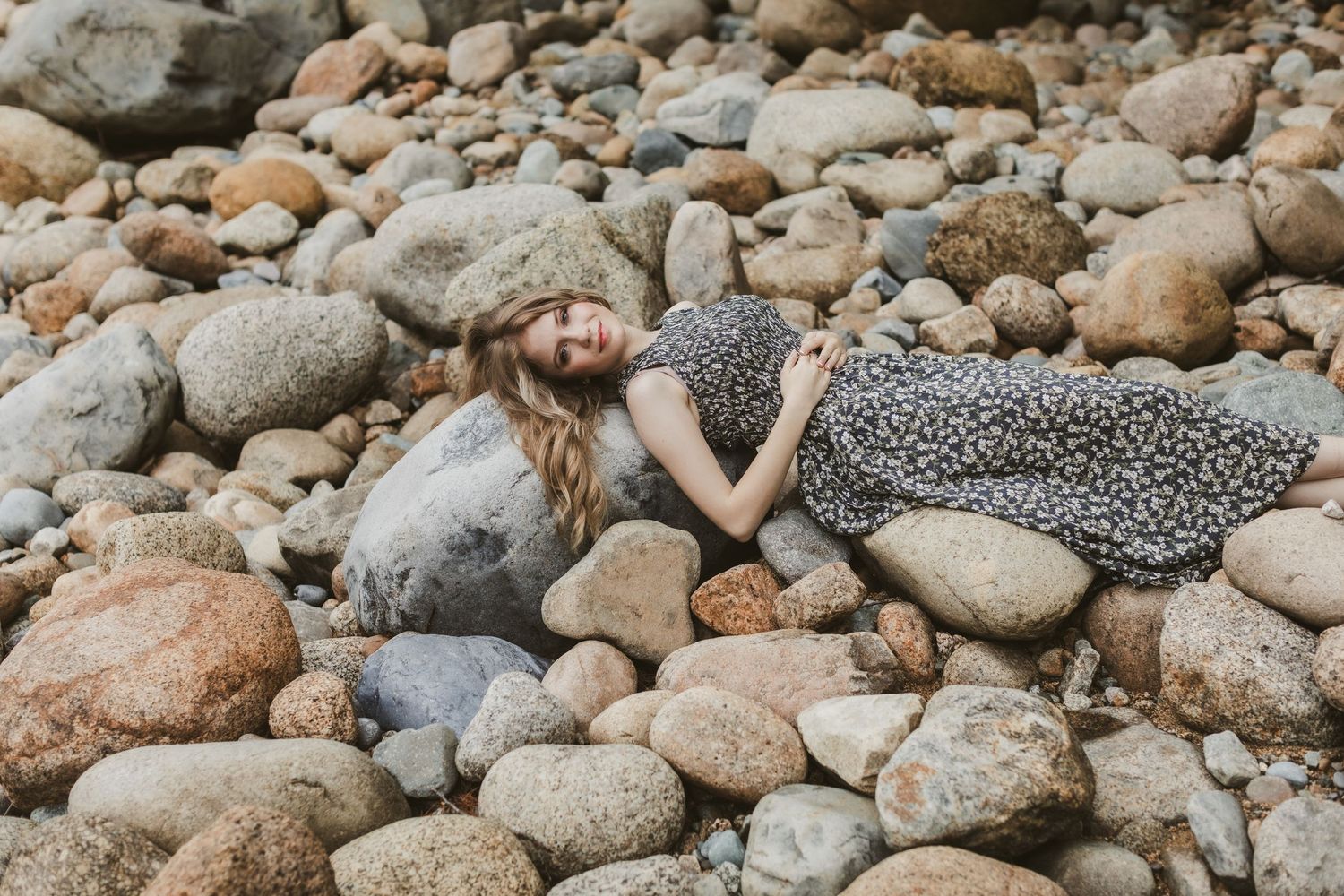 Rachel Delong, Christian musician, wearing a gray floral dress  for a river rock White Mountains Lincoln, New Hampshire photo shoot.