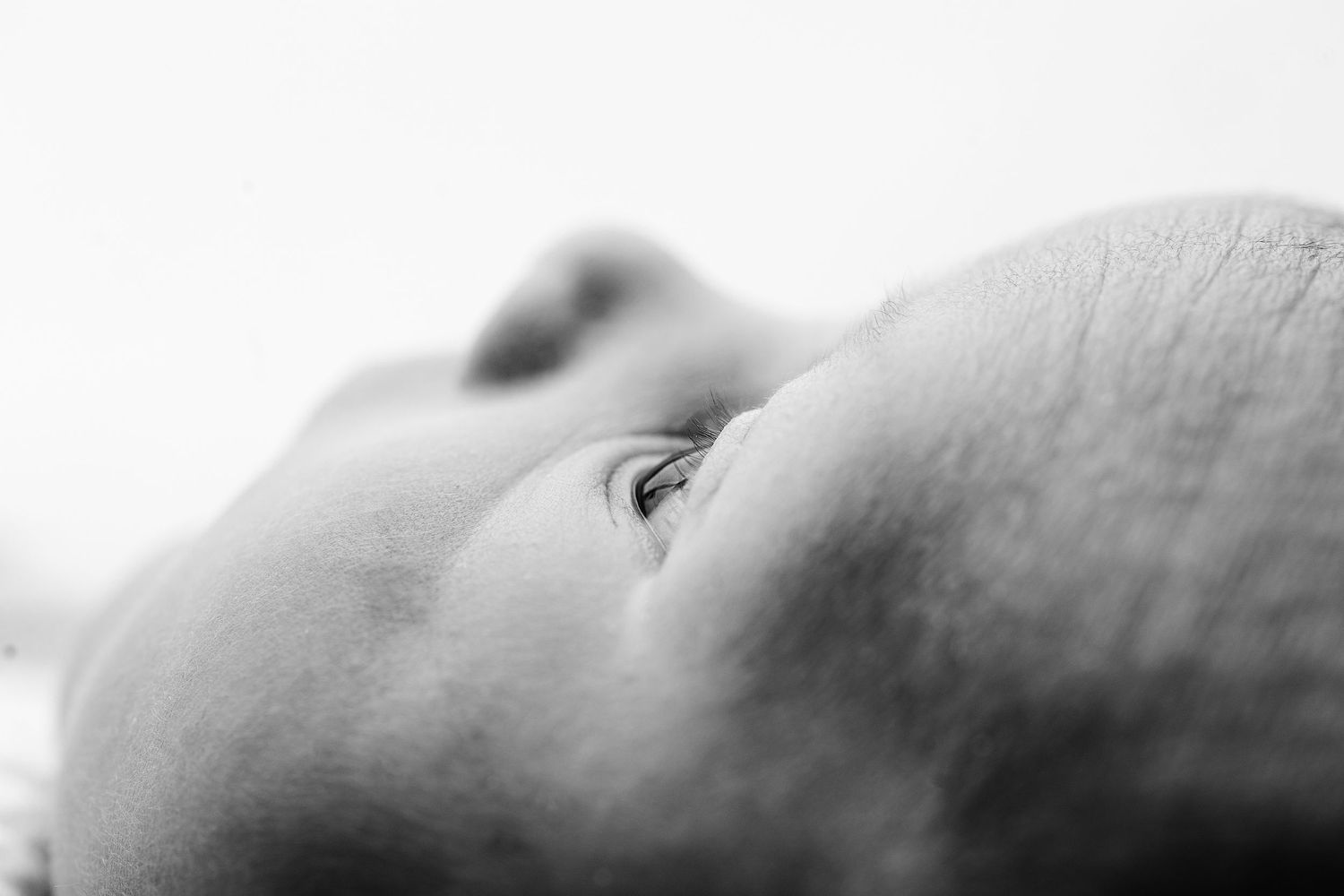Close-up black and white macro photograph showing a baby's eye and profile against a light background.