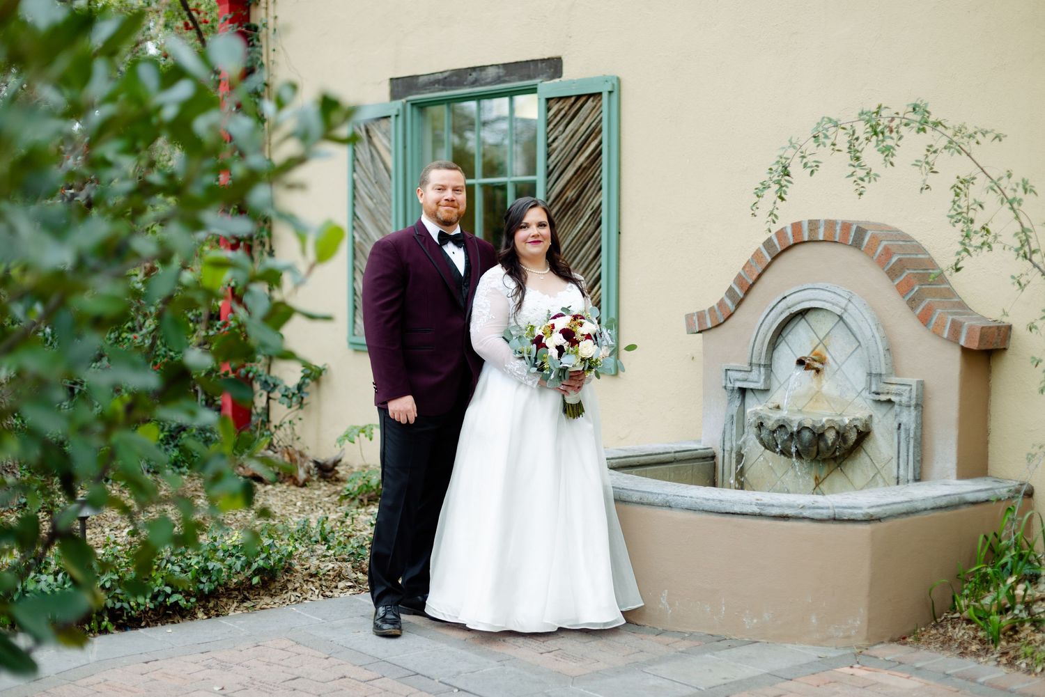 A couple stands beside a decorative stone water fountain at a romantic garden venue.