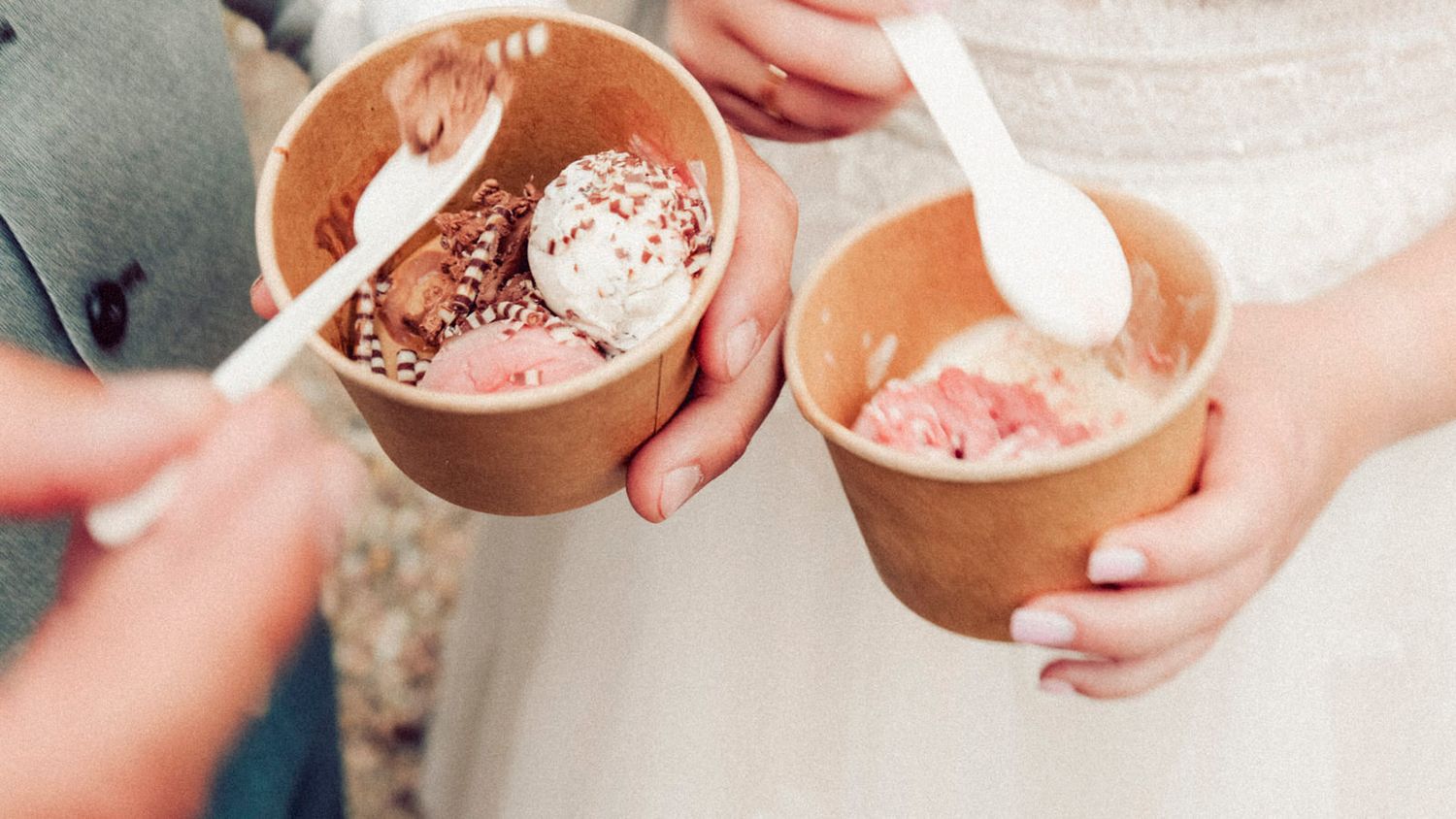 Hands holding clay bowls filled with pink and chocolate smoothies topped with cocoa powder and garnishes.