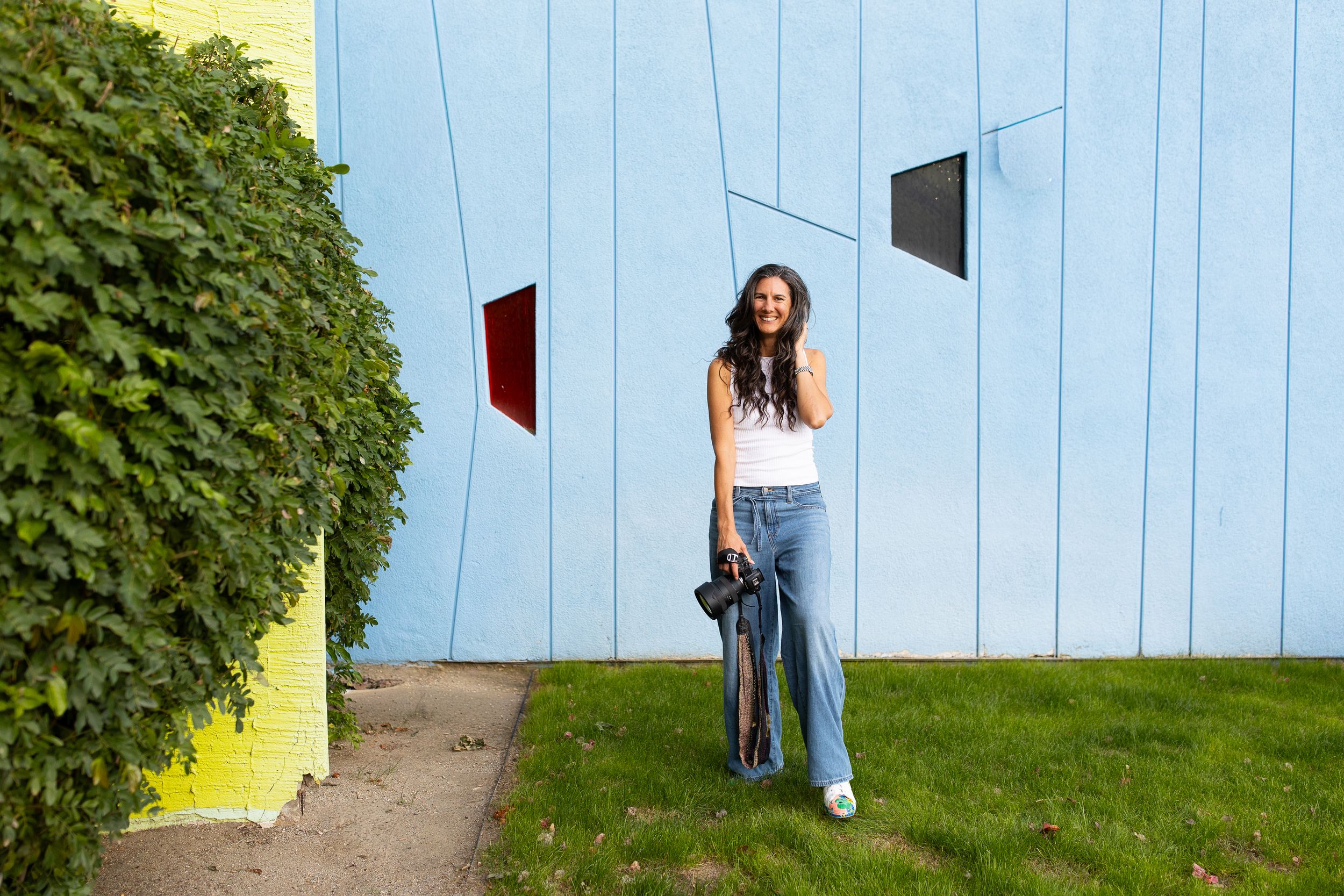 Person peeking playfully from behind blue wall panels in outdoor garden setting.
