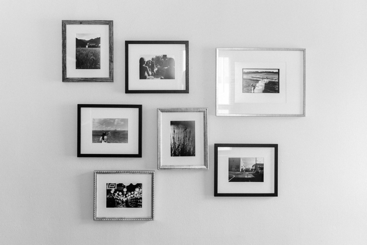 Gallery wall arrangement of seven black and white framed photographs in mixed silver and black frames.