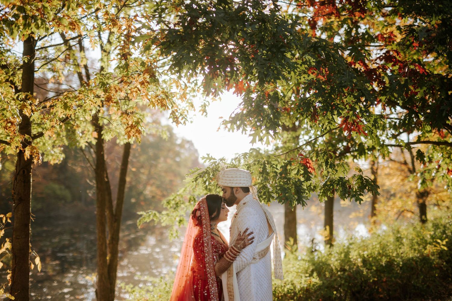 A couple embraces under golden autumn trees during a romantic outdoor photoshoot at sunset.
