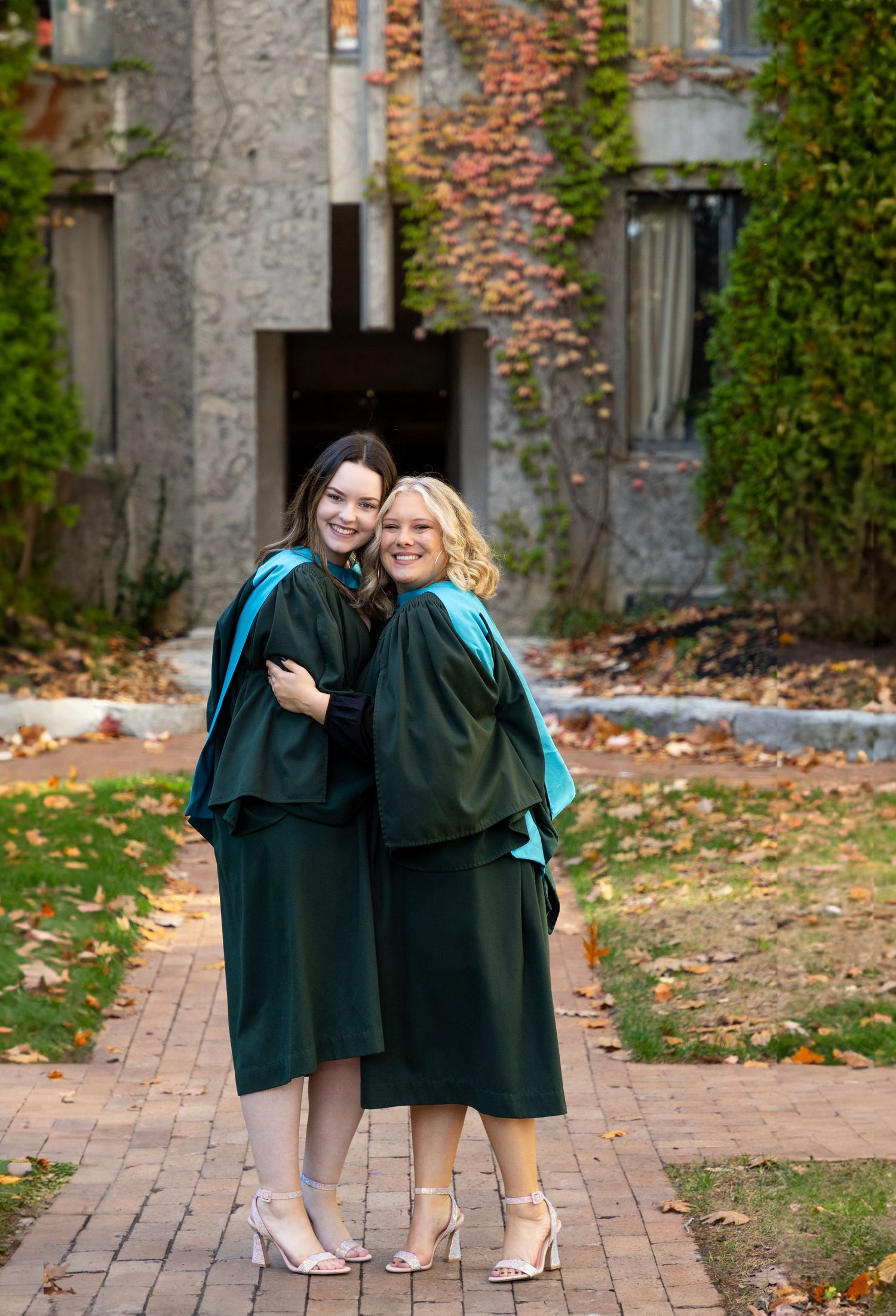 2 graduates hugging each other at the trent champlain campus in the fall wearing their grad gowns