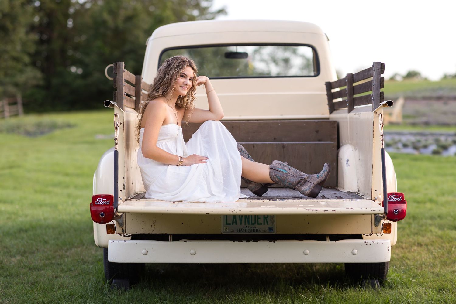 Girl in white sits and poses in the back of a pale yellow pick-up truck for senior photos at Pumpkin Blossom Farm in Warner, New Hampshire