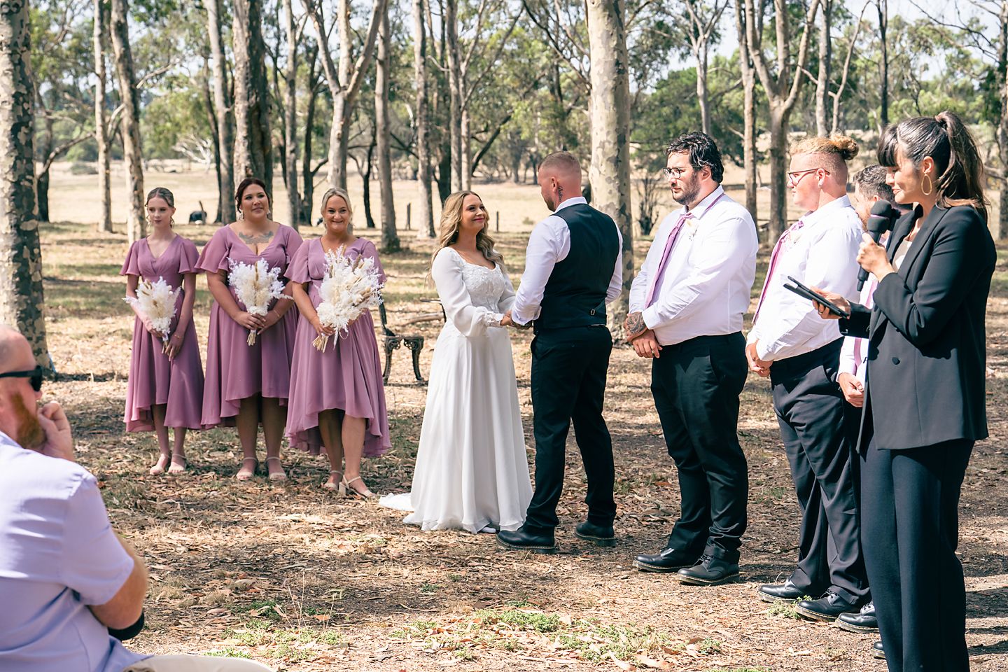 Wedding party stands in a line outdoors among eucalyptus trees wearing pink and black formal attire.
