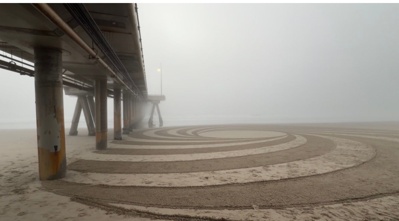A foggy pier stretches into the distance with curved wooden walkways creating a spiral pattern in the mist.