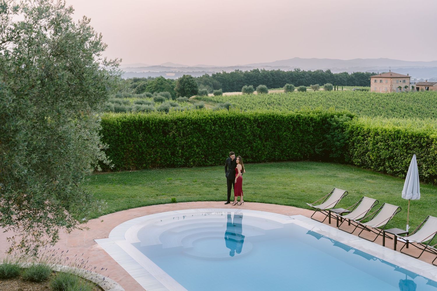 A luxurious infinity pool overlooks rolling hills and countryside with lounge chairs and umbrellas along the deck.
