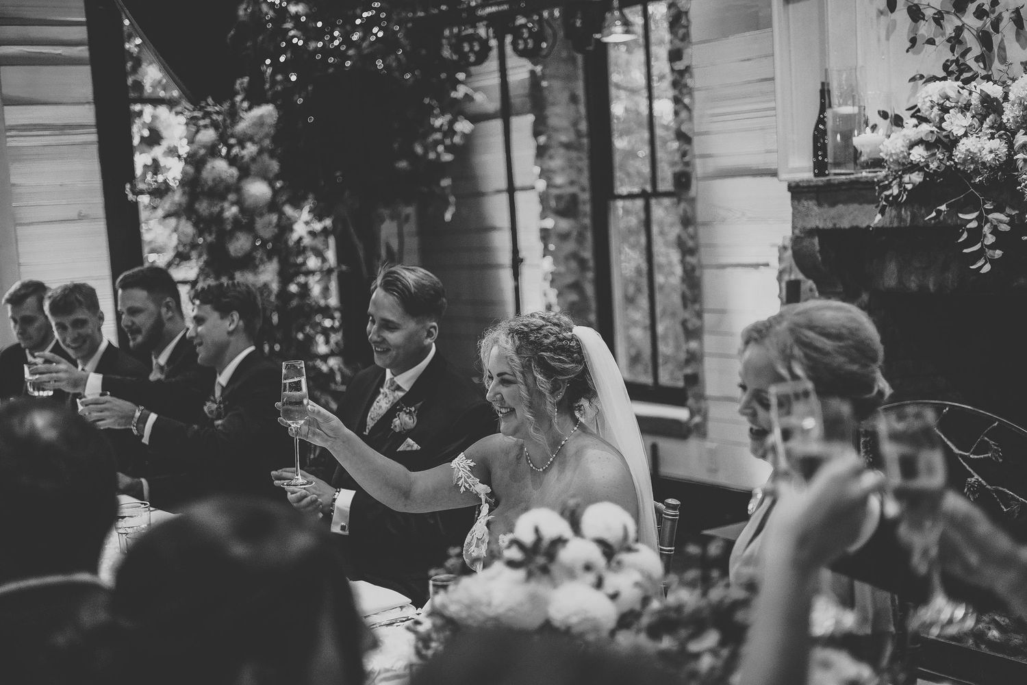 Wedding guests celebrate and toast lifting their glasses during an evening reception at an outdoor venue.