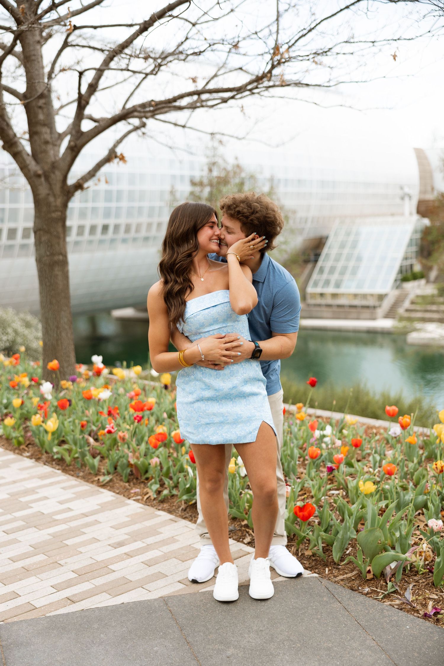 A couple shares an intimate moment among spring tulips near modern architecture.