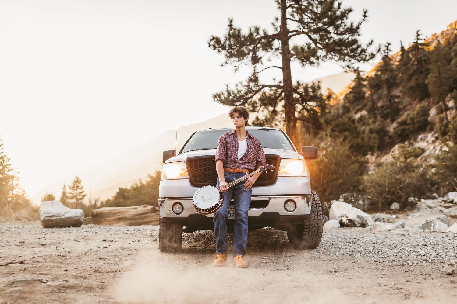A couple sits on a vintage red pickup truck during sunset in a mountainous landscape.