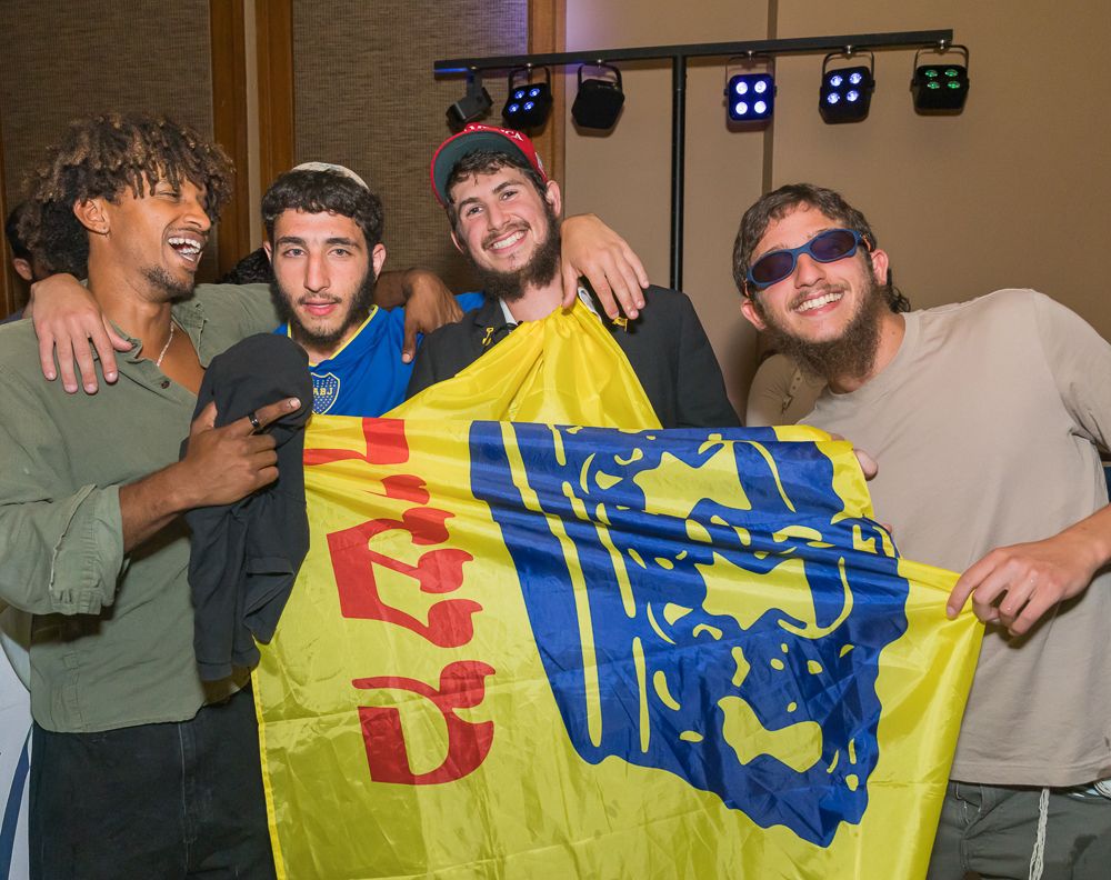 A group of people posing with a yellow and blue flag featuring a logo design in an indoor setting.