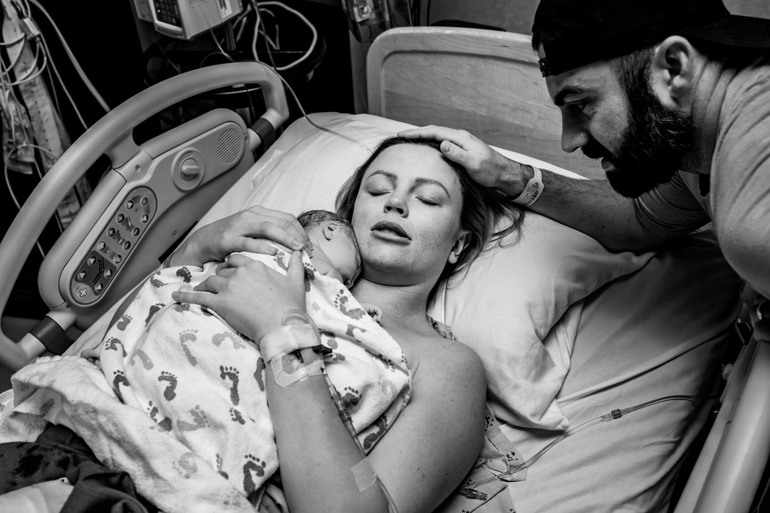New parents admire their newborn baby in a hospital room, with father smiling and mother cradling the infant.