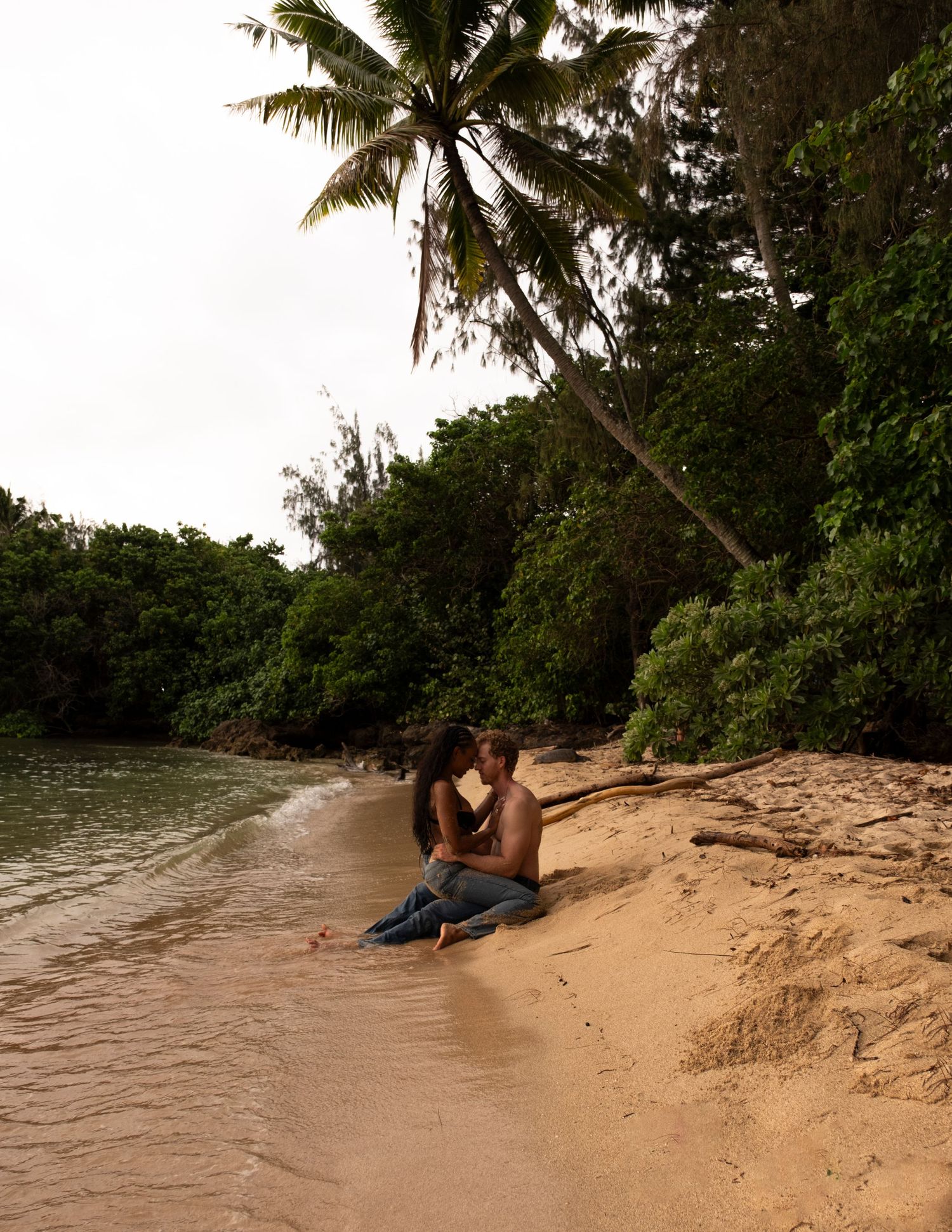 Couple sharing a romantic moment during a North Shore Oahu couples photography session on a tropical beach lined with palm trees.