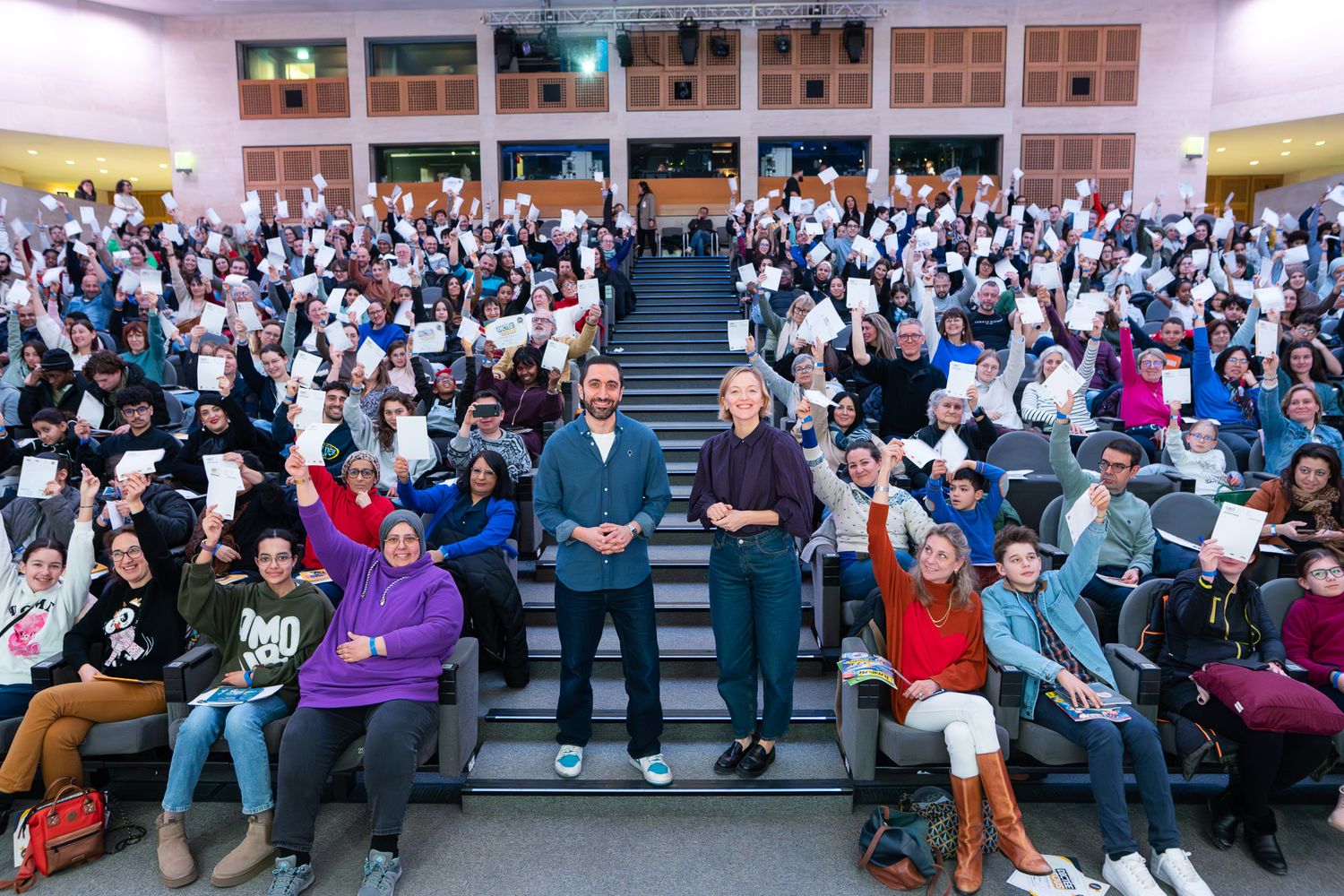 Large crowd of people sitting in rows of seats in an auditorium during what appears to be a presentation or event.