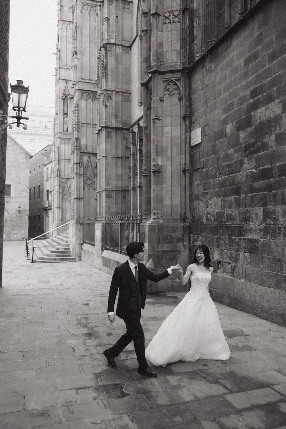 A sequence of black and white wedding photos showing a couple dancing playfully in a historic stone alleyway.