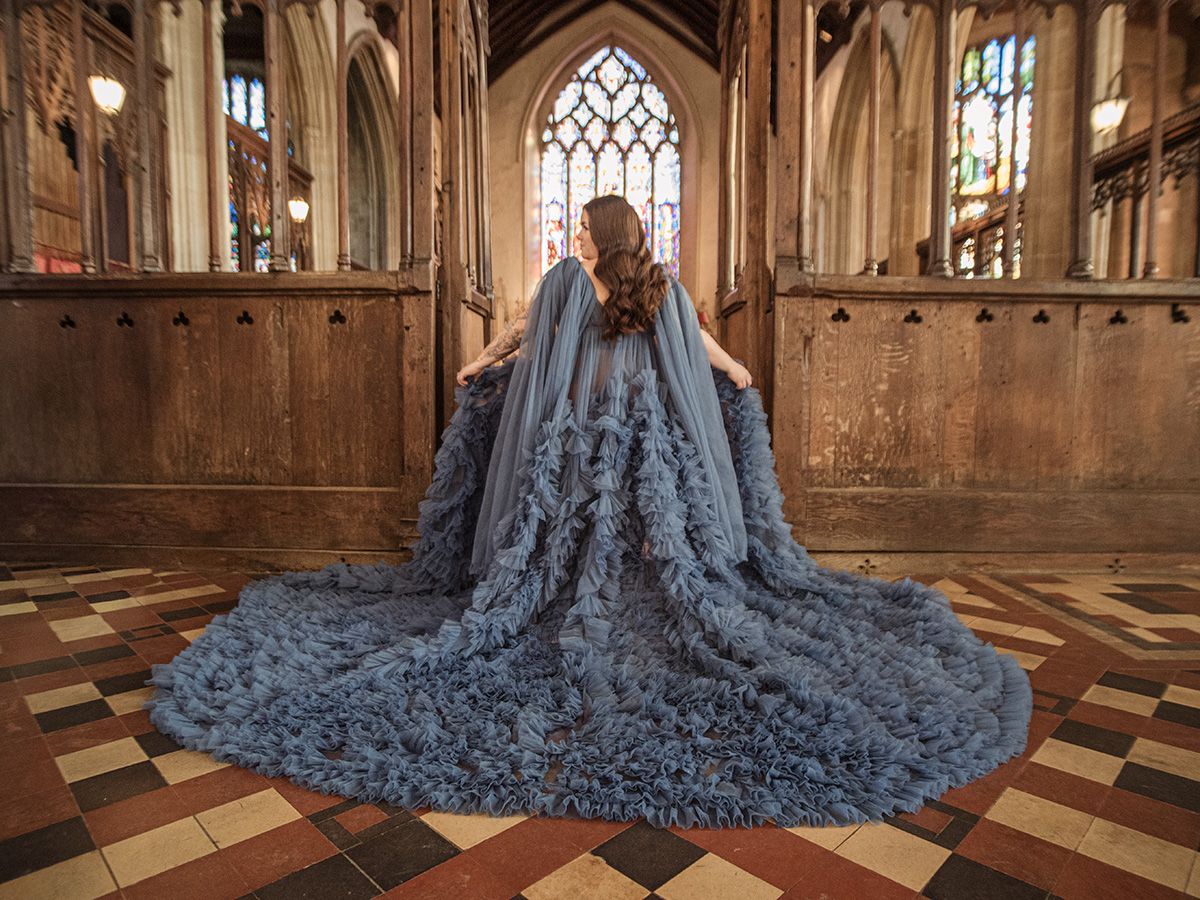 Mum‑to‑be in flowing gown cradling her bump in historic Lavenham St Peter & St Pauls Church, by all scene images photography. Essex, UK.