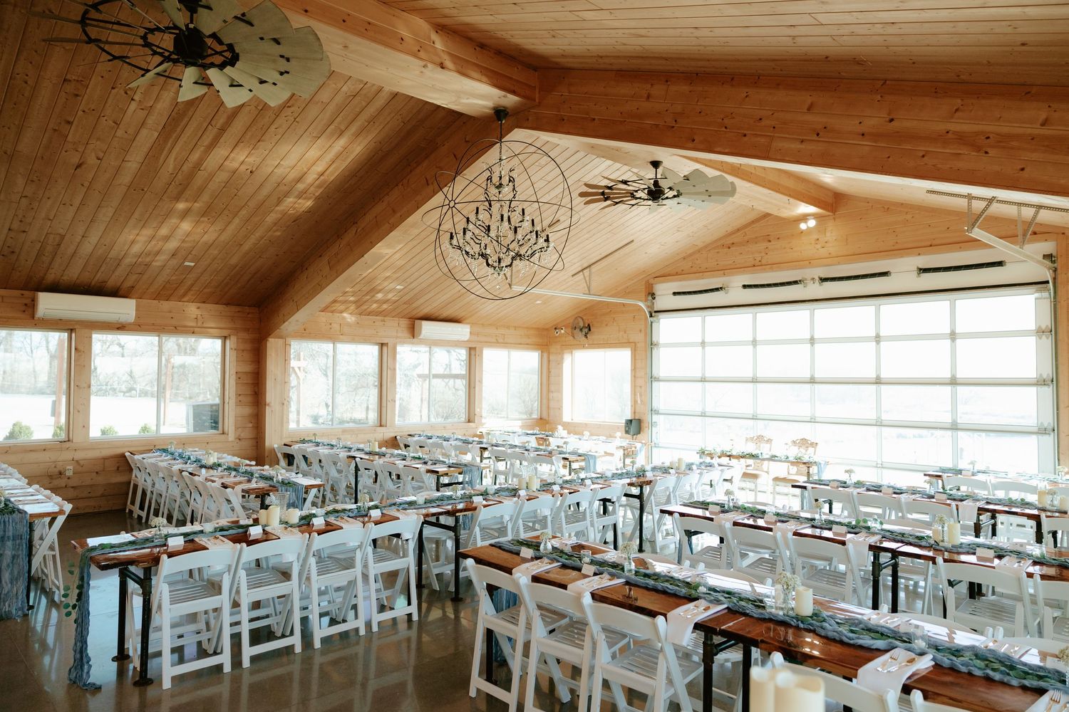 Sparks Barn rustic wedding reception hall with white chairs, wood tables, chandeliers, and large windows in a vaulted cedar ceiling venue.