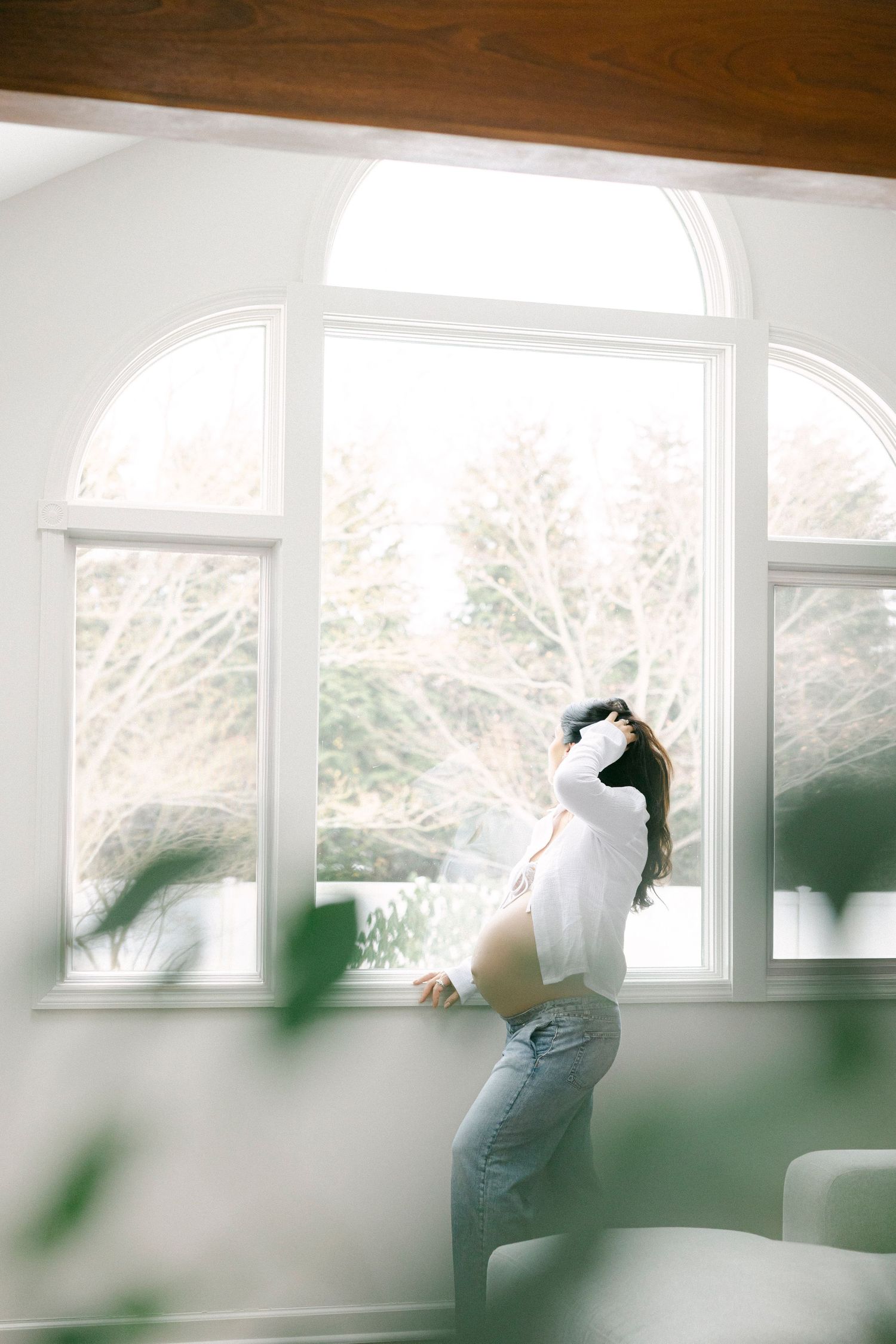 A person in jeans and white top dances gracefully by a large arched window with natural light streaming in.