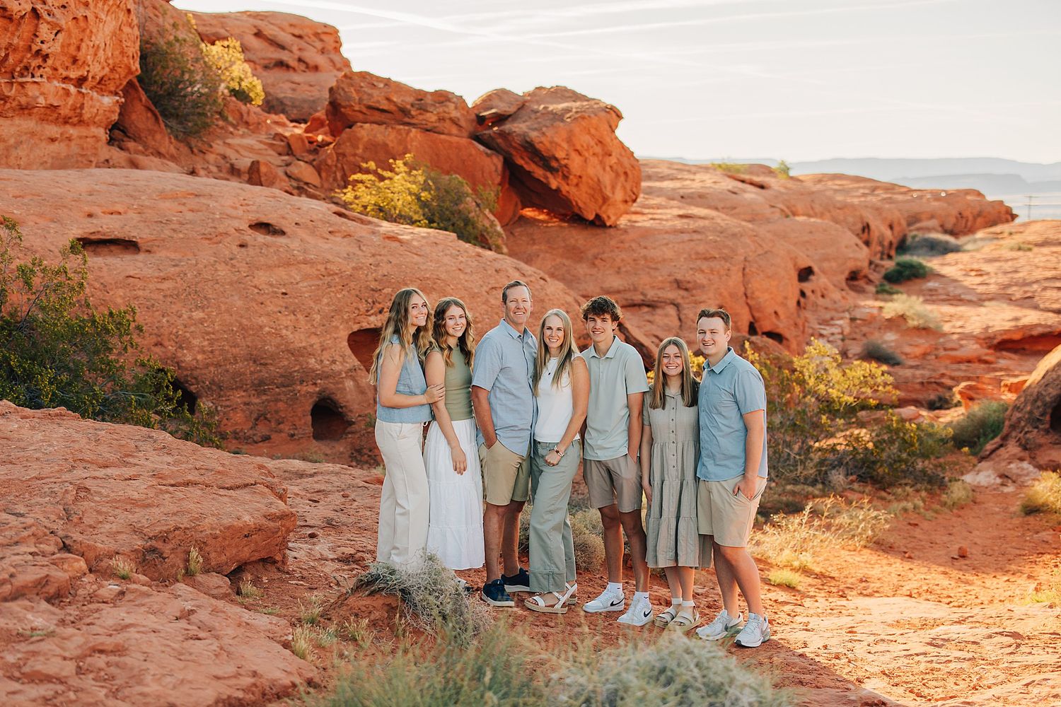 Family of seven posing together on red rock formations at Red Rock Canyon during golden hour sunset.