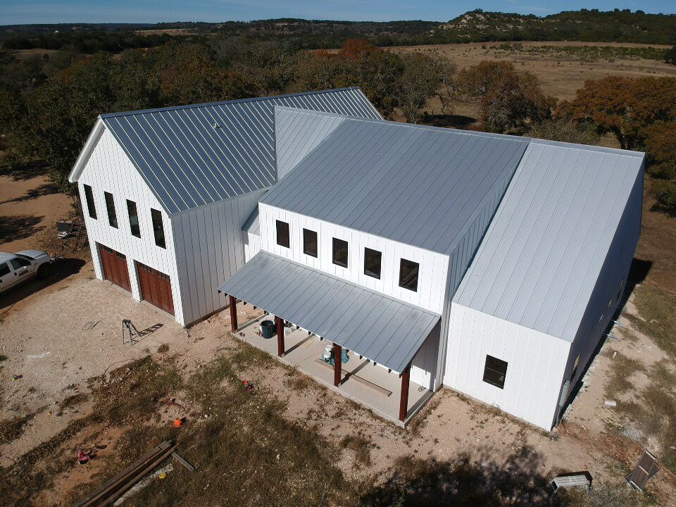 A series of white modern buildings with metal roofs under construction on a rural hillside property.